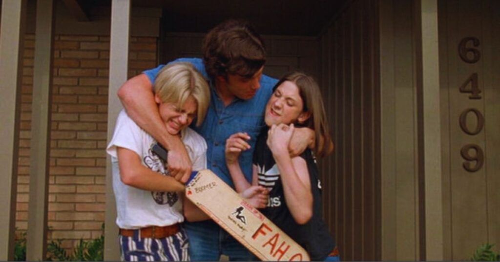 Three friends embrace in front of a house, reminiscent of a heartwarming scene from Dazed and Confused similar to Superbad.